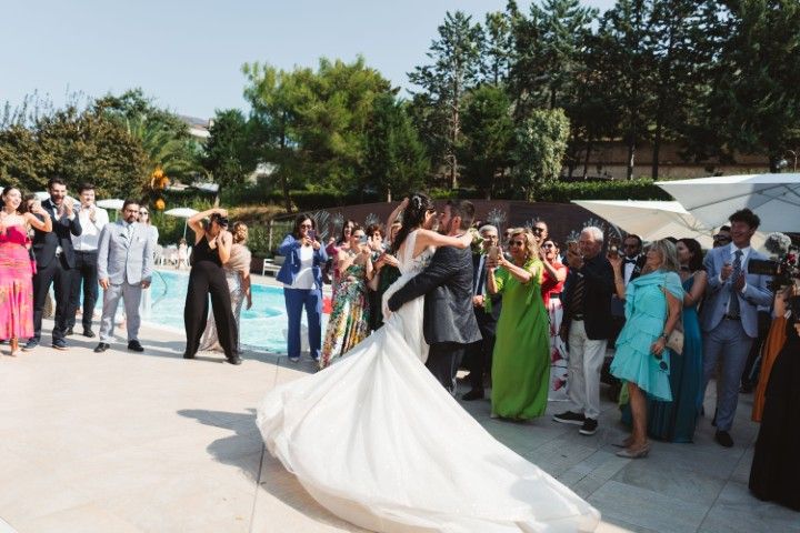 Bride and groom dancing surrounded by applauding guests beside a pool at a wedding reception