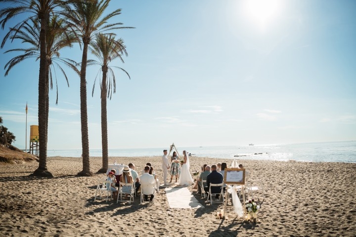 Symbolic beach wedding ceremony in Benalmádena with palm trees, seated guests, and the Mediterranean in the background