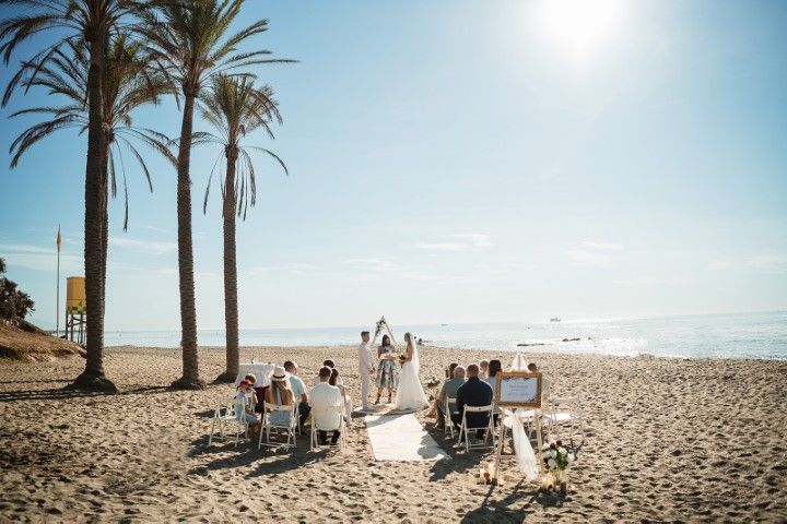 Symbolic beach wedding ceremony in Benalmádena with palm trees, seated guests, and the Mediterranean in the background