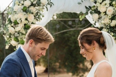 Couple exchanging rings beneath a white floral arch at an outdoor Andalusian wedding ceremony