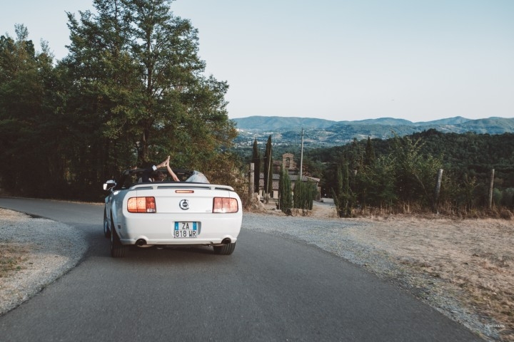 Wedding couple driving through the countryside in a white convertible near a rural Spanish venue